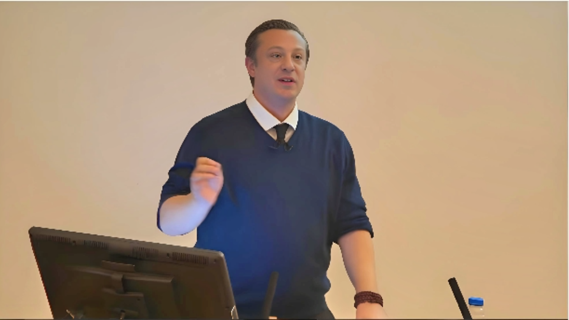 Anton Kreil delivering a lecture on trading in institute of traing depicting Anton Kreil Net Worth 2023, wearing blue shirt, standing near podium