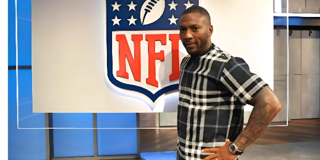 Ryan Clark standin in front of NFL poster wearing black and white shirt smiling beautifully depicting marvelous career and Ryan Clark net worth